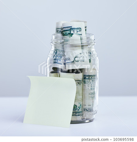 Save up, you dont know what lies ahead. a blank note and a jar filled with money against a grey background. Save up, you dont know what lies ahead. a blank note and a jar filled with money against a grey background. 103695598