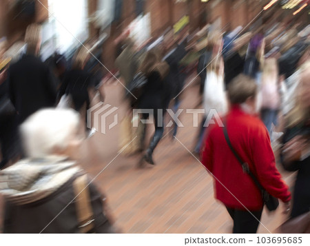 A group of people commuting through urban roads with blurred motion. A busy crowd of travelers arriving and walking together in a street in the city. Lots of tourists in defocused movement downtown 103695685