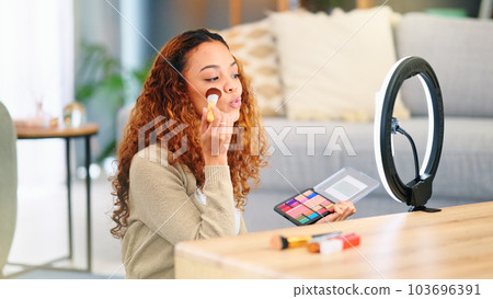 Beauty influencer filming a makeup tutorial at home. Young female blogger live streaming a broadcast online with ring light for a vlog channel. Recording a fun podcast for followers on social media 103696391