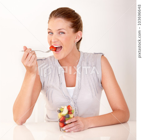 Woman, eating portrait and fruit salad in a studio with happiness from healthy breakfast and food. Smile, young female person and diet nutrition of a model with organic fruits for wellness and health 103696648