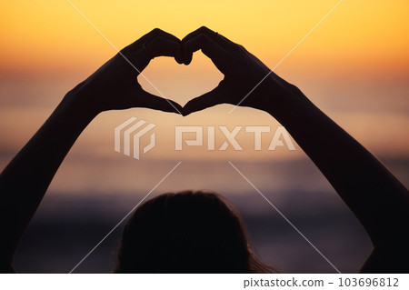 Appreciate your own existence. a unrecognizable female holding a heart shape with her fingers while doing yoga at the beach. 103696812