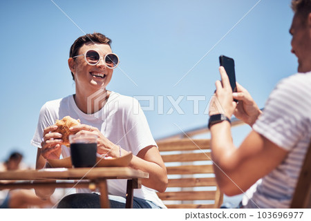 Hold still while a take a photo. a cheerful young woman getting her picture taken by her boyfriend outside while they have lunch. 103696977