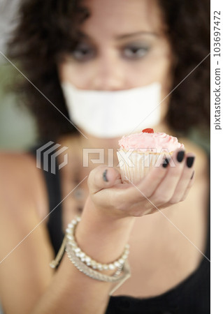 Cupcake in hand, eating disorder and a woman on diet and tape over mouth to stop or lose weight. Face, covering and restriction of female suffering with anorexia, body dysmorphia or bulimia problem 103697472
