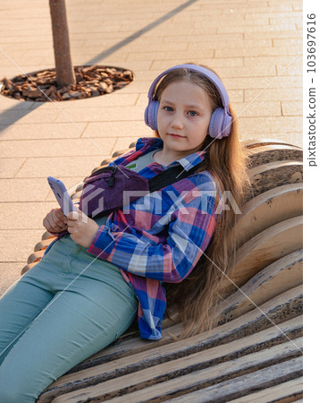 Blonde child in headphones listening to music podcast smartphone outside Young girl learn online lesson enjoy audio book Blonde child in headphones listening to music podcast smartphone outside Young girl learn online lesson enjoy audio book 103697616