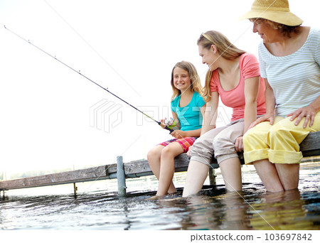 Im going to catch me a huge one. A little girl fishing with her grandmother and mother while sitting on a jetty by the lake. Im going to catch me a huge one. A little girl fishing with her grandmother and mother while sitting on a jetty by the lake. 103697842
