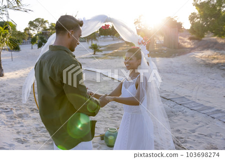 Caucasian newlywed couple holding hands and standing at beach at wedding ceremony, copy space 103698274