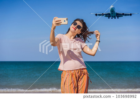 Woman makes a selfie on the beach watching the landing planes. Traveling on an airplane concept. Text space. Island Phuket in Thailand. Impressive paradise. Hot beach Mai Khao. Amazing landscape 103698992
