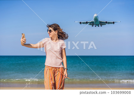 Woman makes a selfie on the beach watching the landing planes. Traveling on an airplane concept. Text space. Island Phuket in Thailand. Impressive paradise. Hot beach Mai Khao. Amazing landscape 103699008