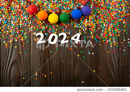 White numbers 2024 and color sugar sprinkles on wooden table with color balls garland White numbers 2024 and color sugar sprinkles on wooden table with color balls garland 103699481