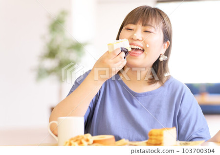 A young woman happily eating a cake 103700304