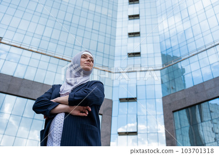 Portrait of a pregnant business woman in a hijab and a suit with crossed arms on her chest outdoors. 103701318