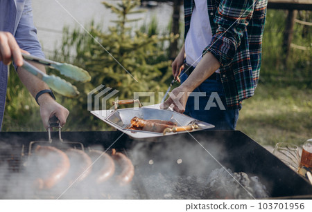 The men are grilling sausages on the barbecue enjoys picnic by the lake. The men are grilling sausages on the barbecue enjoys picnic by the lake. 103701956