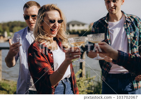 Energetic charged girl smiles to friends on the shore of the lake drink wine. 103702067