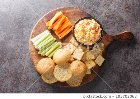 Pimento or pimiento cheese is a spread made of cheese, mayonnaise and pimientos and served on crackers and vegetables closeup on the wooden board. Horizontal top view 103702068