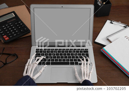 Human skeleton in suit using laptop at table, closeup Human skeleton in suit using laptop at table, closeup 103702205
