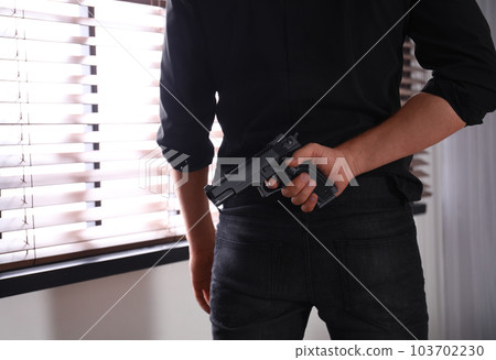 Man with gun near window indoors, closeup Man with gun near window indoors, closeup 103702230