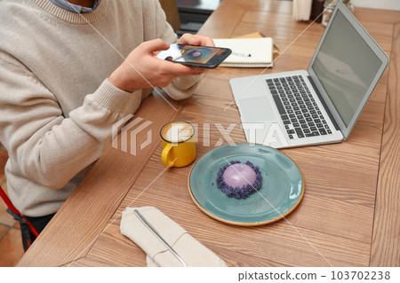 Male blogger taking photo of dessert and coffee at table in cafe, closeup 103702238