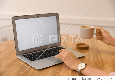 Young blogger with cup of coffee working at table in cafe, closeup 103702247