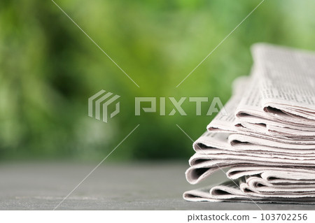 Stack of newspapers on grey table against blurred green background, space for text. Journalist's work 103702256