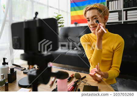 Young queer man beauty make up artist or vlogger recording makeup tutorial in home studio. LGBTQ lifestyle, influencer, blogger Young queer man beauty make up artist or vlogger recording makeup tutorial in home studio. LGBTQ lifestyle, influencer, blogger 103703260