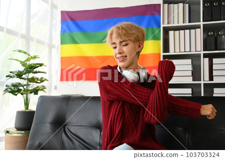 Happy young gay man relaxing on couch at home with closed eyes, stretching arms. LGBTQ, people lifestyle, leisure concept 103703324