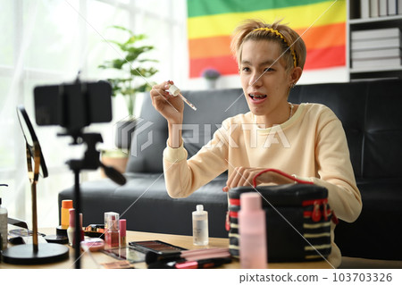 Young queer man beauty make up artist or vlogger recording makeup tutorial in home studio. LGBTQ lifestyle, influencer, blogger Young queer man beauty make up artist or vlogger recording makeup tutorial in home studio. LGBTQ lifestyle, influencer, blogger 103703326