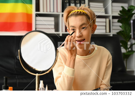 Young asian man applying concealer under his eyes with cosmetics brush. LGBTQ lifestyle, beauty and cosmetic Young asian man applying concealer under his eyes with cosmetics brush. LGBTQ lifestyle, beauty and cosmetic 103703332