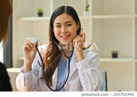 Positive female doctor in white coat holding stethoscope and looking at camera. Healthcare and medical concept 103703340