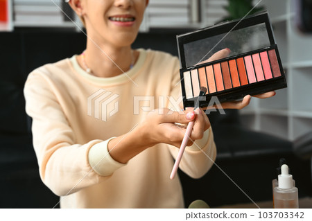 Young gay man influencer, makeup artist holding palette of colorful eye shadows, recording product review for vlog Young gay man influencer, makeup artist holding palette of colorful eye shadows, recording product review for vlog 103703342