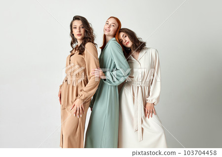 Tender femininity. Beautiful young women, friends in elegant dresses posing together against light studio background Tender femininity. Beautiful young women, friends in elegant dresses posing together against light studio background 103704458