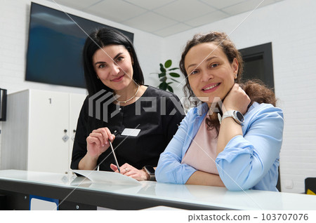 Beautiful woman, confident dentist doctor, dental hygienist or female orthodontist and her happy pregnant patient ,smiling looking at camera, standing at reception counter in modern dental clinic Beautiful woman, confident dentist doctor, dental hygienist or female orthodontist and her happy pregnant patient ,smiling looking at camera, standing at reception counter in modern dental clinic 103707076