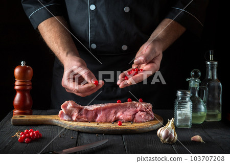 In the restaurant kitchen chef prepares raw calf meat. Before baking, the cook puts the viburnum on the beef. National dish 103707208