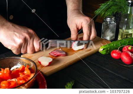 Chef cuts radishes in a vegetable salad. Cooking delicious salad in the kitchen of a restaurant or cafe 103707226