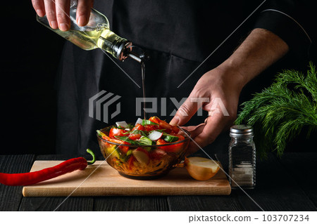 Cook pours olive oil into a bowl of salad. Cooking tasty and healthy food with set of vitamins Cook pours olive oil into a bowl of salad. Cooking tasty and healthy food with set of vitamins 103707234