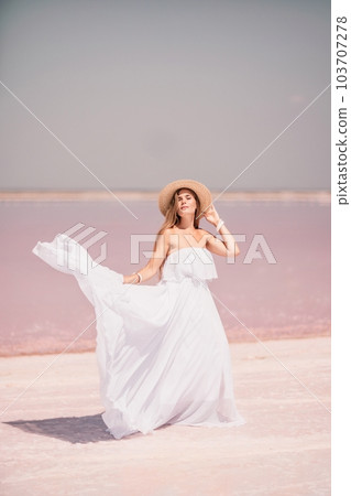 Woman in pink salt lake. She in a white dress and hat enjoys the scenic view of a pink salt lake as she walks along the white, salty shore, creating a lasting memory. Woman in pink salt lake. She in a white dress and hat enjoys the scenic view of a pink salt lake as she walks along the white, salty shore, creating a lasting memory. 103707278