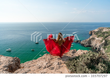 Woman sea red dress yachts. A beautiful woman in a red dress poses on a cliff overlooking the sea on a sunny day. Boats and yachts dot the background. Woman sea red dress yachts. A beautiful woman in a red dress poses on a cliff overlooking the sea on a sunny day. Boats and yachts dot the background. 103707297