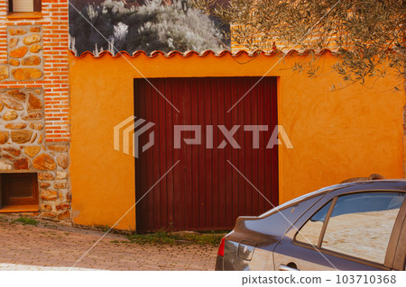 Bright orange garage door and car parked at the gate of a private home. Terracotta brick wall outside in a residential neighborhood. Warehouse exterior. Entrance to a house, building. Bright orange garage door and car parked at the gate of a private home. Terracotta brick wall outside in a residential neighborhood. Warehouse exterior. Entrance to a house, building. 103710368