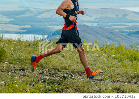 male runner running marathon trail race in background of mountains and lake, summer ultramarathon 103710432