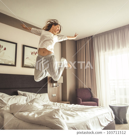 Woman having fun and jumping with bathrobe on bed in hotel room 103711512