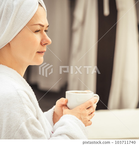 Woman in white bathrobe and towel lying on sofa and relaxing with tea at the roof. 103711740