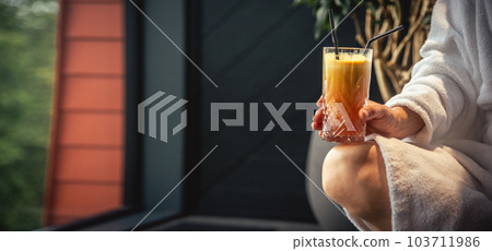 Woman in white bathrobe lying on sofa and relaxing with orange cocktail at home. Woman in white bathrobe lying on sofa and relaxing with orange cocktail at home. 103711986