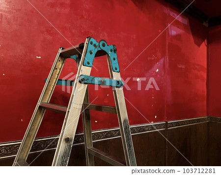 A stepladder placed in front of a red wall A stepladder placed in front of a red wall 103712281