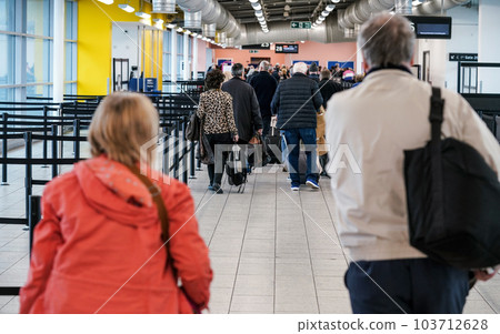 Group of anonymous people at airport gate line to board an airplane, queue crowd, pulling their trolley seen from behind. 103712628