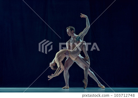 Muscular young man and beautiful woman, ballet dancers making artistic performance, dancing against blue studio background 103712748