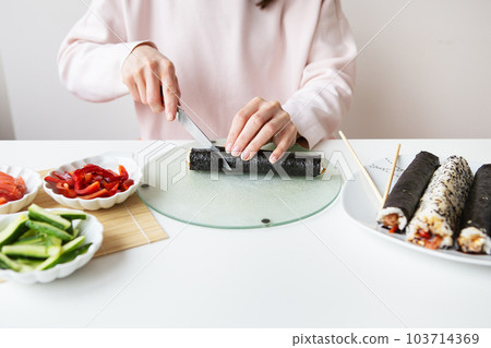 The process of making sushi, the girl makes sushi with different flavors - fresh salmon, caviar, avocado, cucumber, ginger, rice. Cut the roll into pieces. 103714369