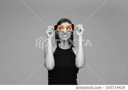 Black and white image of young girl holding colorful photo part, model expressing anger and irritation. Creative collage. 103714429
