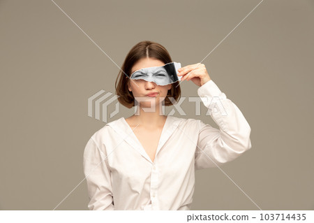 Young girl with funny grimace face holding photo part with eyes looking attentively. Creative collage. 103714435