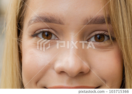 Extreme close-up macro portrait of young face, blonde woman's eyes looking at camera, smiling 103715366