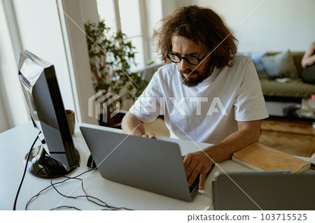 Thoughtful man freelancer sitting at desk and working at laptop and computer in home office 103715525