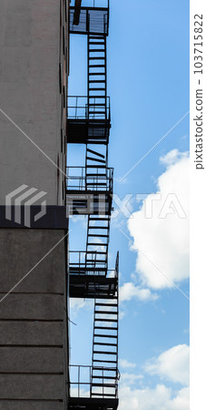 Silhouette of a fire escape on a high-rise building against a blue sky 103715822